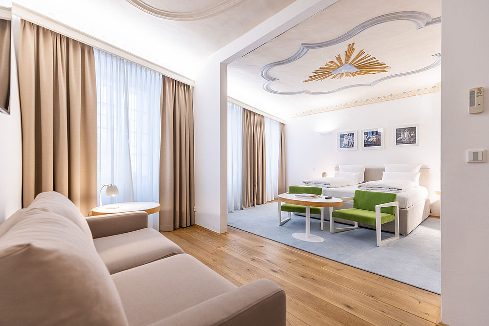 Ein lichtdurchflutetes Hotelzimmer in weißen und goldenen Farben mit einer schönen Couch und einem großen Bett