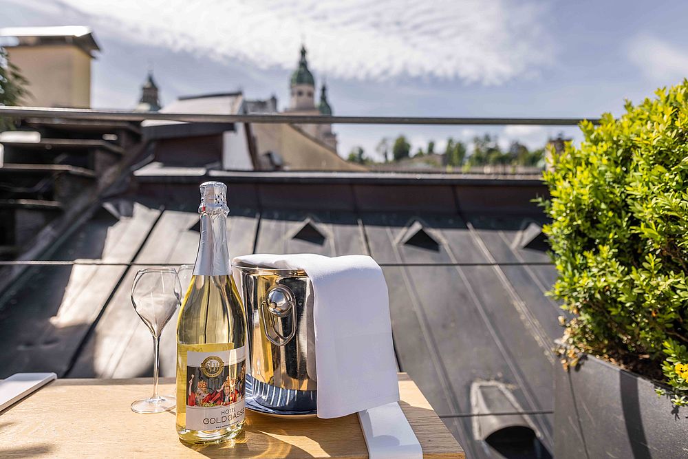 Eine Weißweinflasche des Hotel Goldgasse inklusive Glas und Eimer stehen auf dem Dach des Hotels
