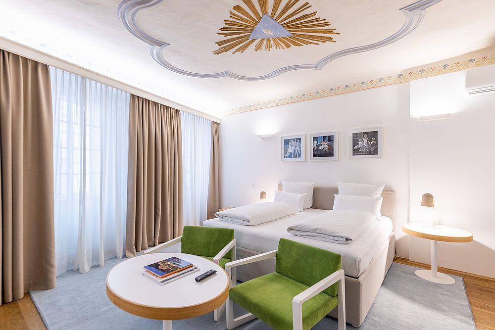 Ein großes Bett in einem weitläufigen Zimmer im Hotel Goldgasse mit großen Fenstern