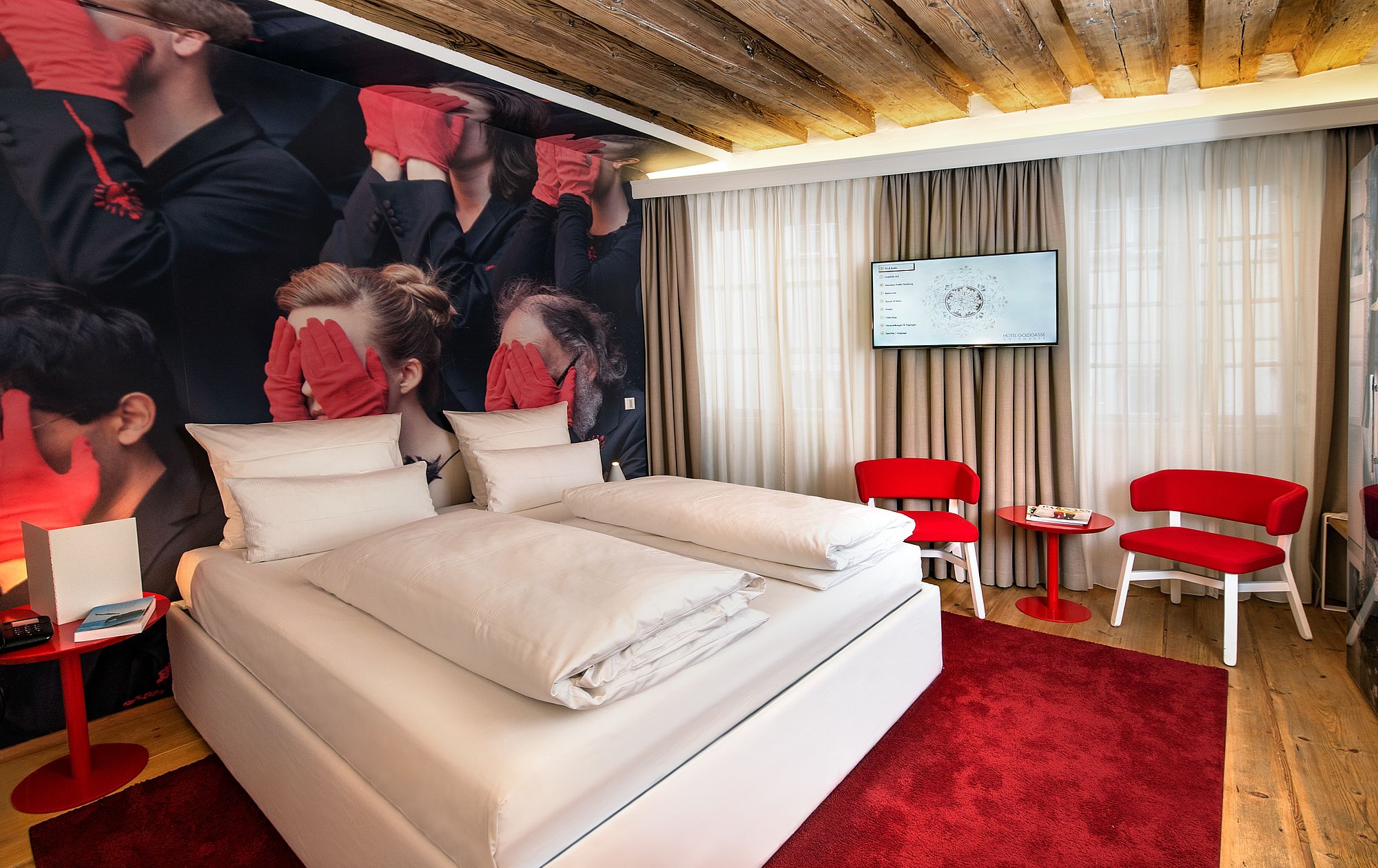 Gemütliches Doppelbett mit roten Teppich und Fernseher an der Wand im romantischen Hotel Salzburg