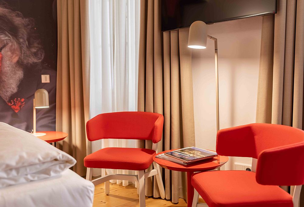 Zwei rot-orangene Stühle und eine Stehlampe in einer Ecke eines Hotelzimmers