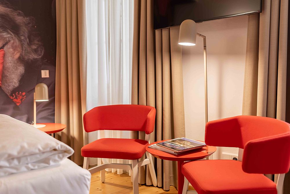 Zwei rot-orangene Stühle und eine Stehlampe in einer Ecke eines Hotelzimmers