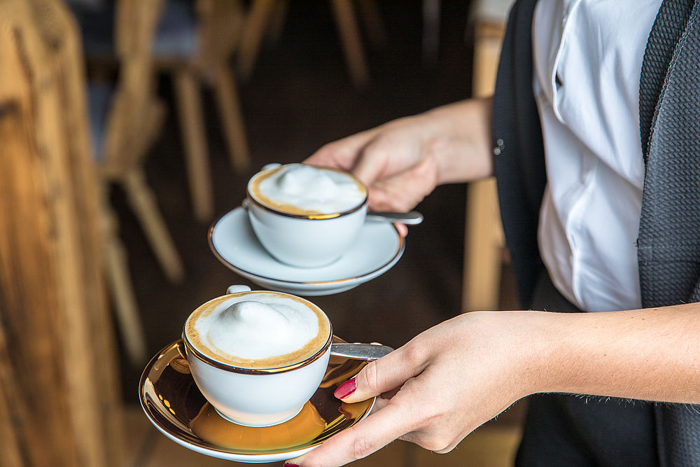 Kellnerin des Boutique Hotel Salzburg serviert Gästen zwei Cappuccino