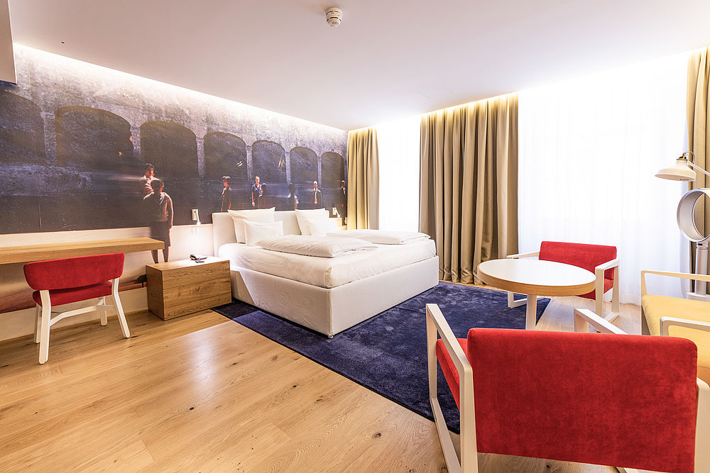 Juniorsuite mit vielen roten Stühlen und einem gemütlichen Doppelbett im Boutique Hotel Salzburg